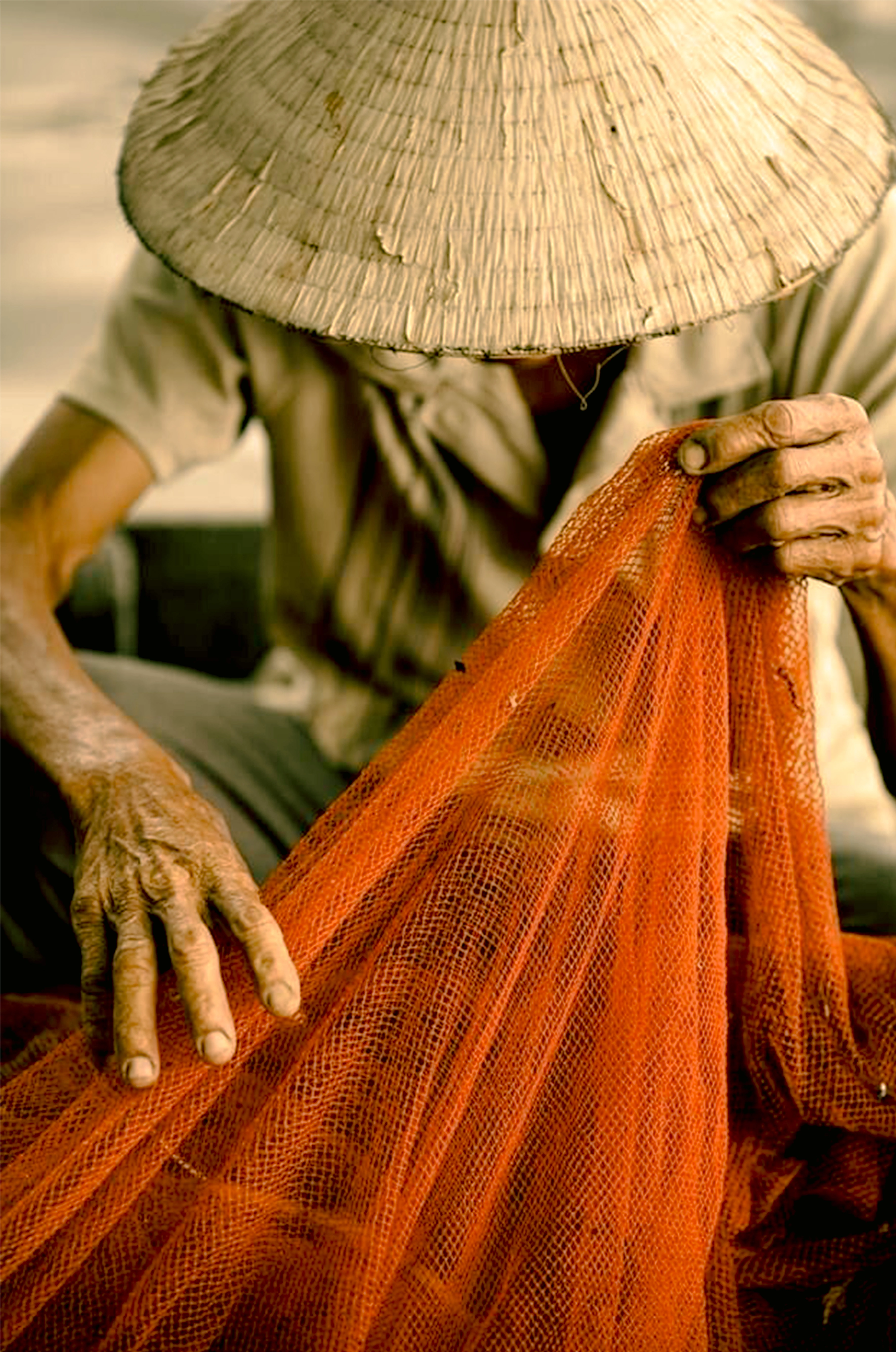 Artesano local asiático con sombrero cónico tradicional trabajando con una red de pesca, mostrando una conexión profunda con la cultura del destino.