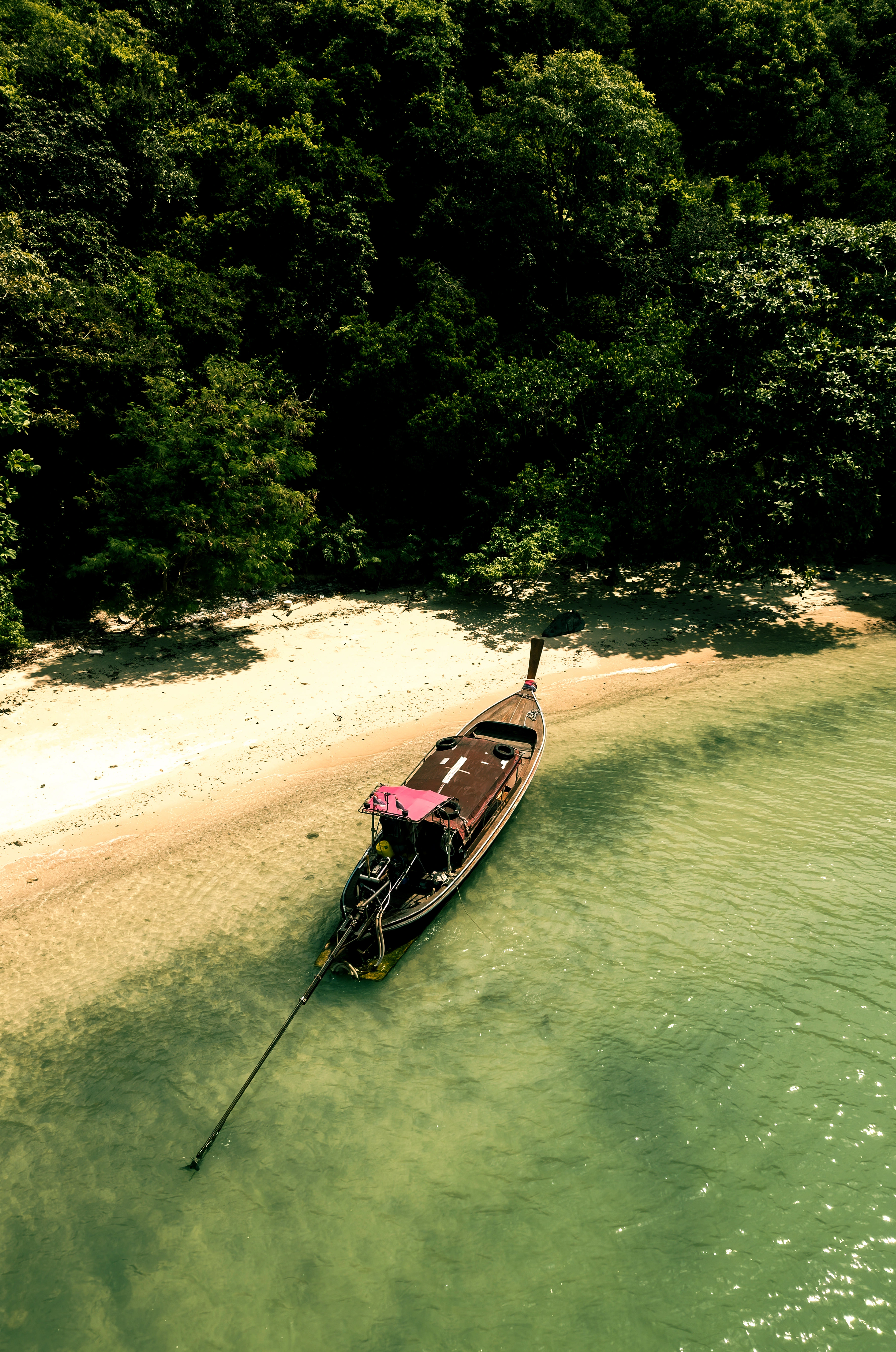 Barca tradicional de madera anclada en aguas cristalinas junto a una playa virgen y solitaria durante una ruta exclusiva por Asia.